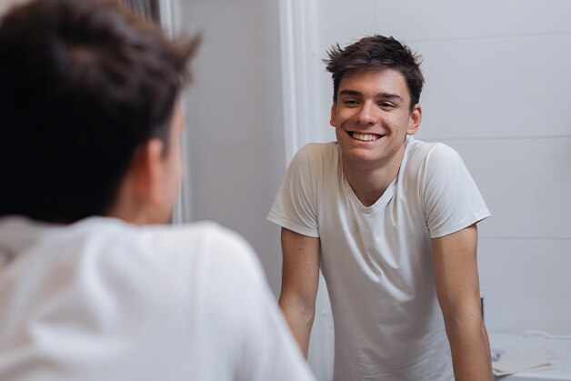 Joven de camiseta blanca sonriendo frente al espejo